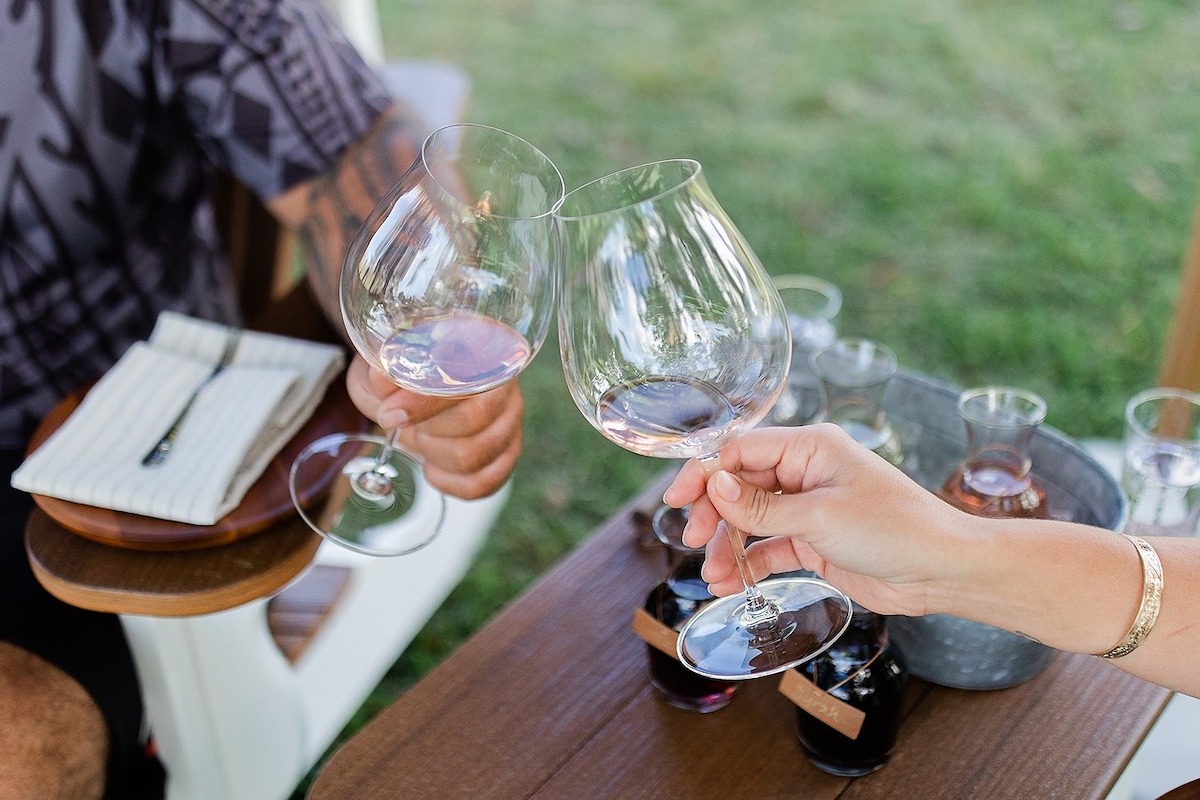 Two people hold wine glasses above a brown table with wine tasting cards and other glasses of wine.