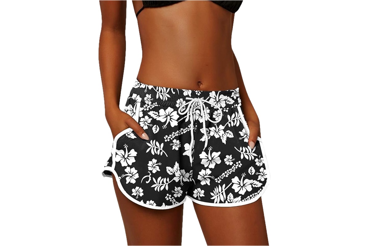 The lower body of a woman dressed in black and white floral board shorts.