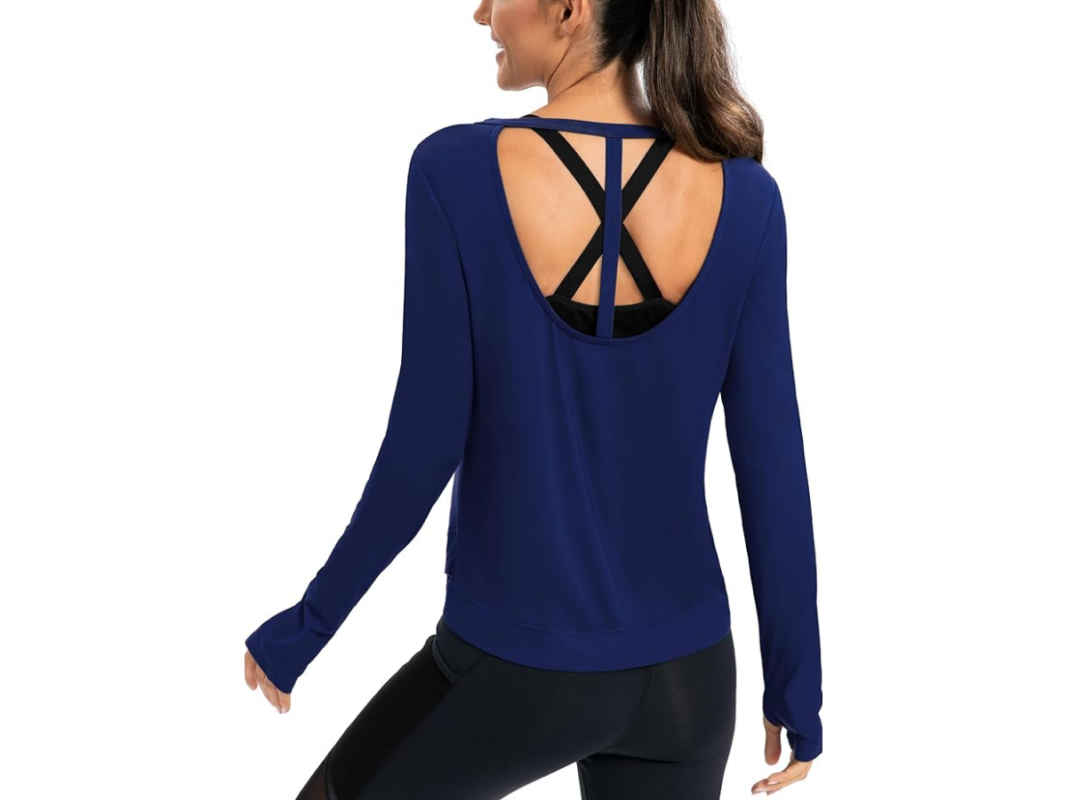 This image features the upper body of a woman, back towards us, wearing a blue long sleeve workout top with an open back and a T design at the neckline