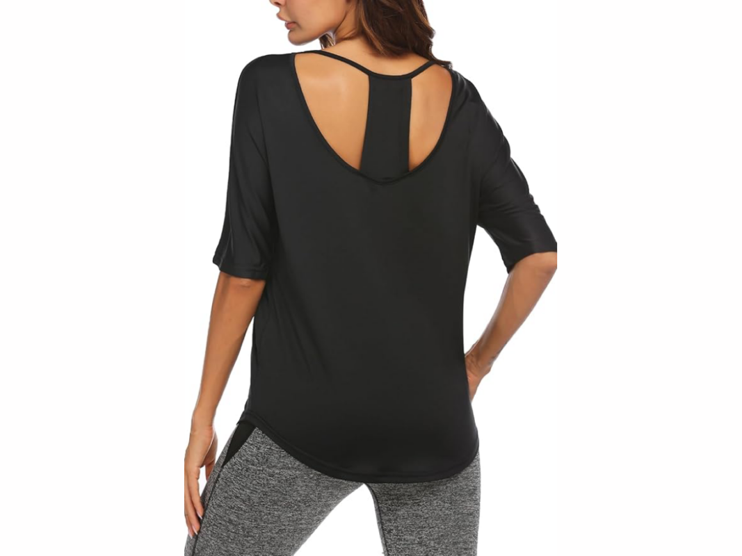 This image features a woman with her back to us. She is wearing a short sleeve, black top with a T shape feature and scooped back. She is wearing grey pants.