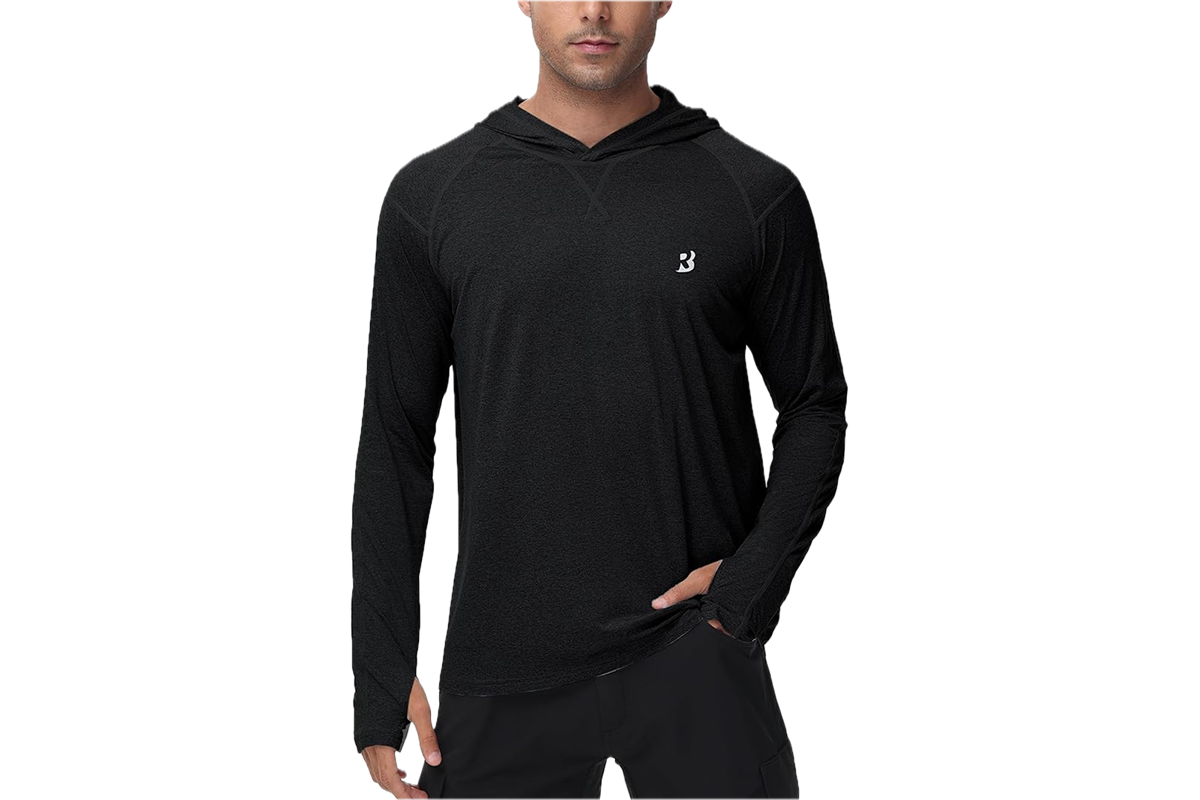 This photo features a man wearing a long sleeve t shirt with thumbholes and a hood. There is a white design on the upper left chest. He is wearing black pants.