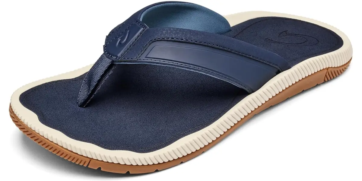 A dark blue flip-flop sandal for men with a white and brown sole. The sandal features a thick strap with a rounded logo near the center and a soft-looking footbed for comfort. The outsole has a textured pattern for grip.