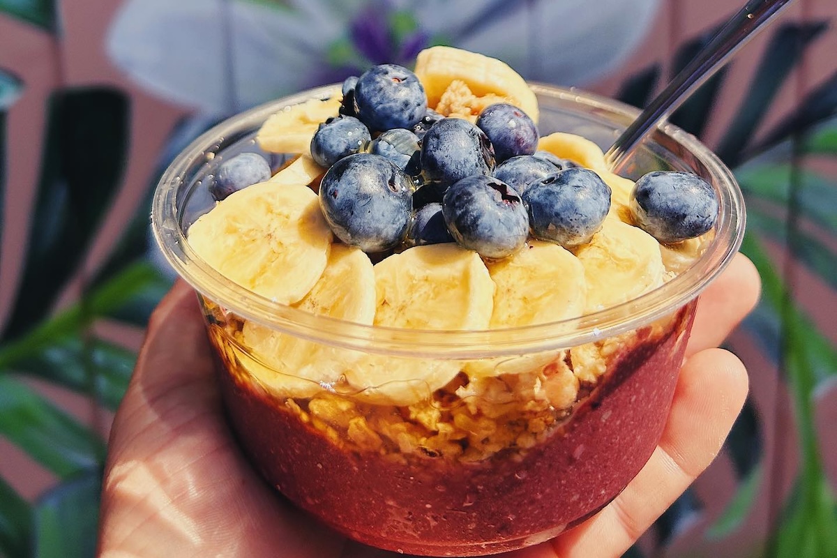 Someone holds an acai bowl topped with granola, honey, blueberries and bananas.