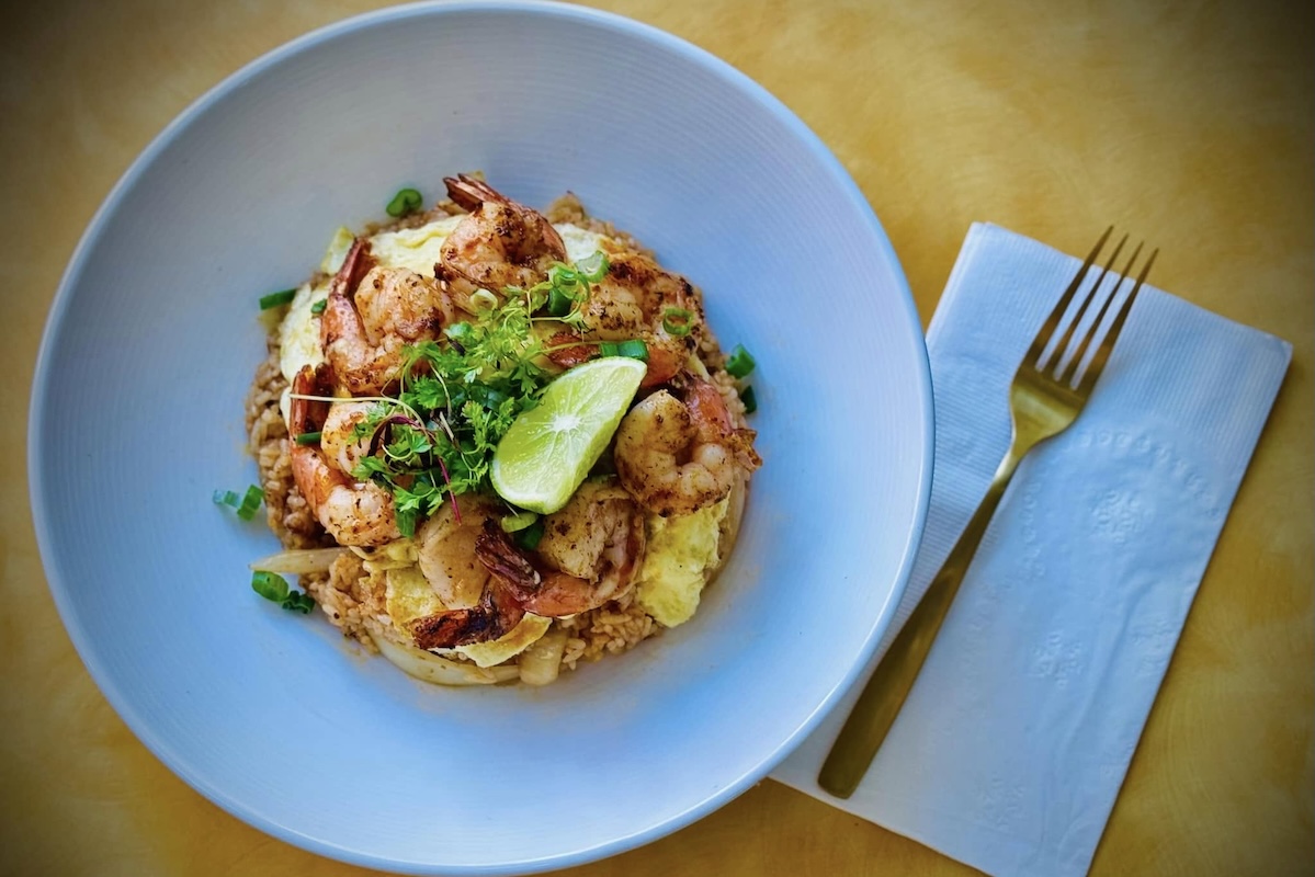A plate of rice with prawns, lime and cilantro.