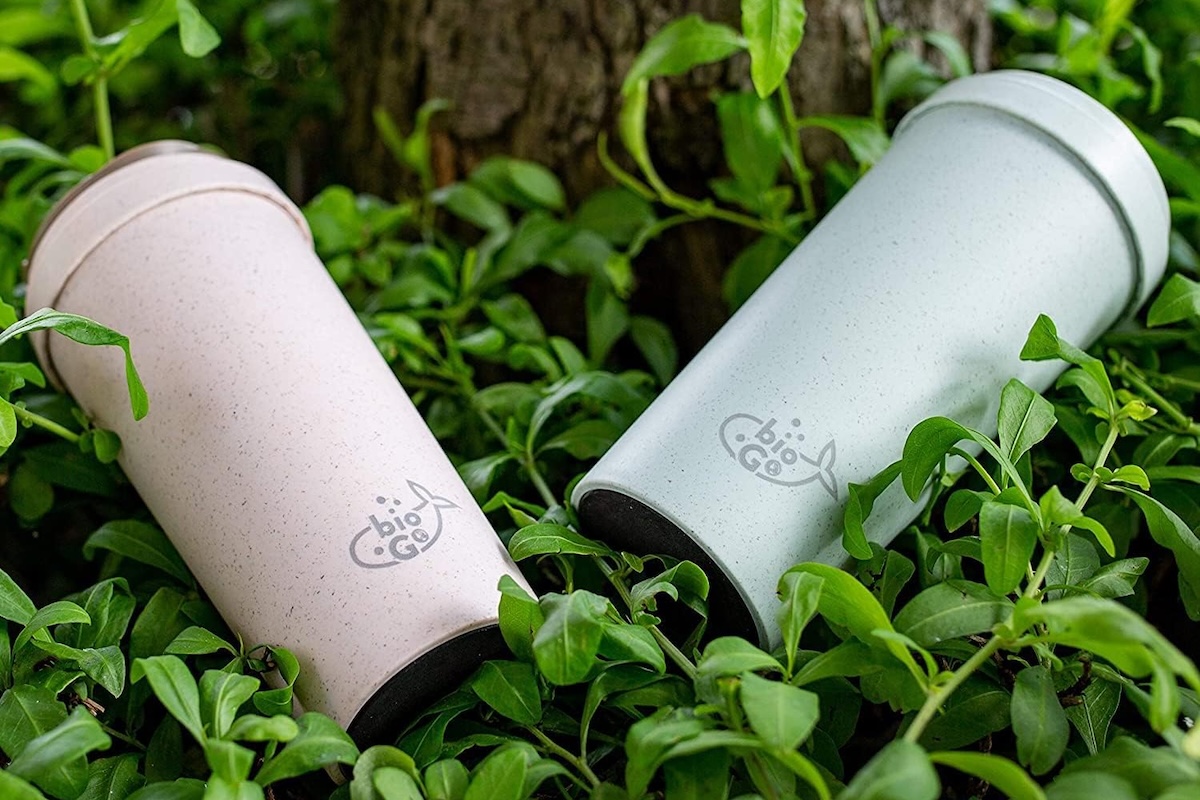 Pink and blue travel coffee cups sitting in a bed of green leaves.