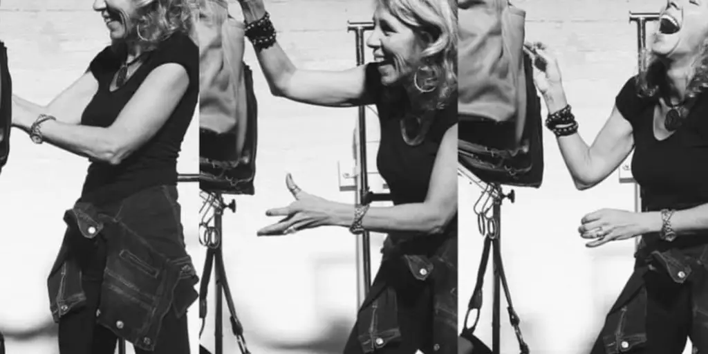 A black-and-white triptych by Lynn Tallerico shows a woman in three panels, engaged in animated conversation. She wears a short-sleeve top and has a jacket tied around her waist. Her expressive gestures suggest excitement or enthusiasm. Studio equipment is visible in the background.