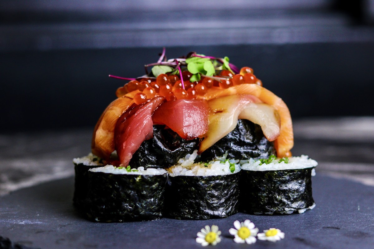 Sushi rolls are stacked with some raw fish, fish roe and sprouts on top.