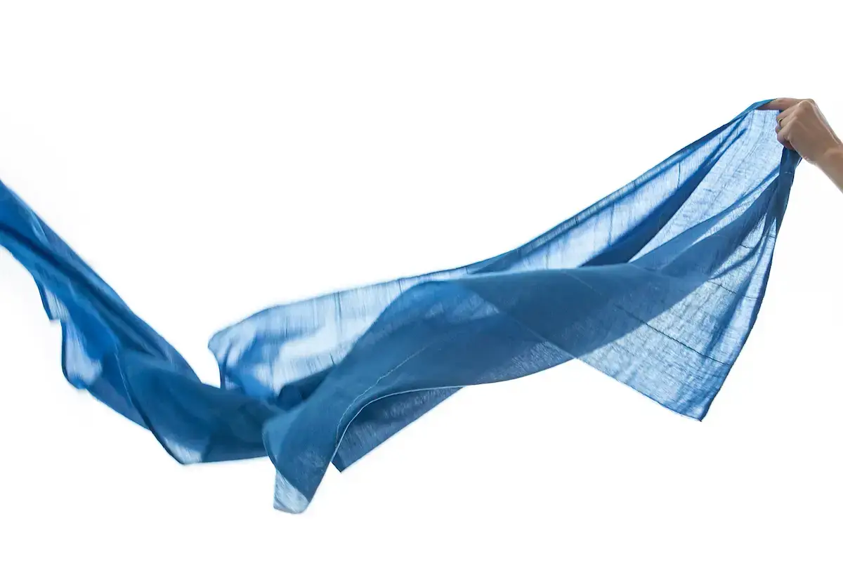 A hand holding a flowing blue scarf against a white background. The scarf billows gracefully, capturing a sense of movement and lightness—an embodiment of the Shoo for Good ethos in every gentle wave.