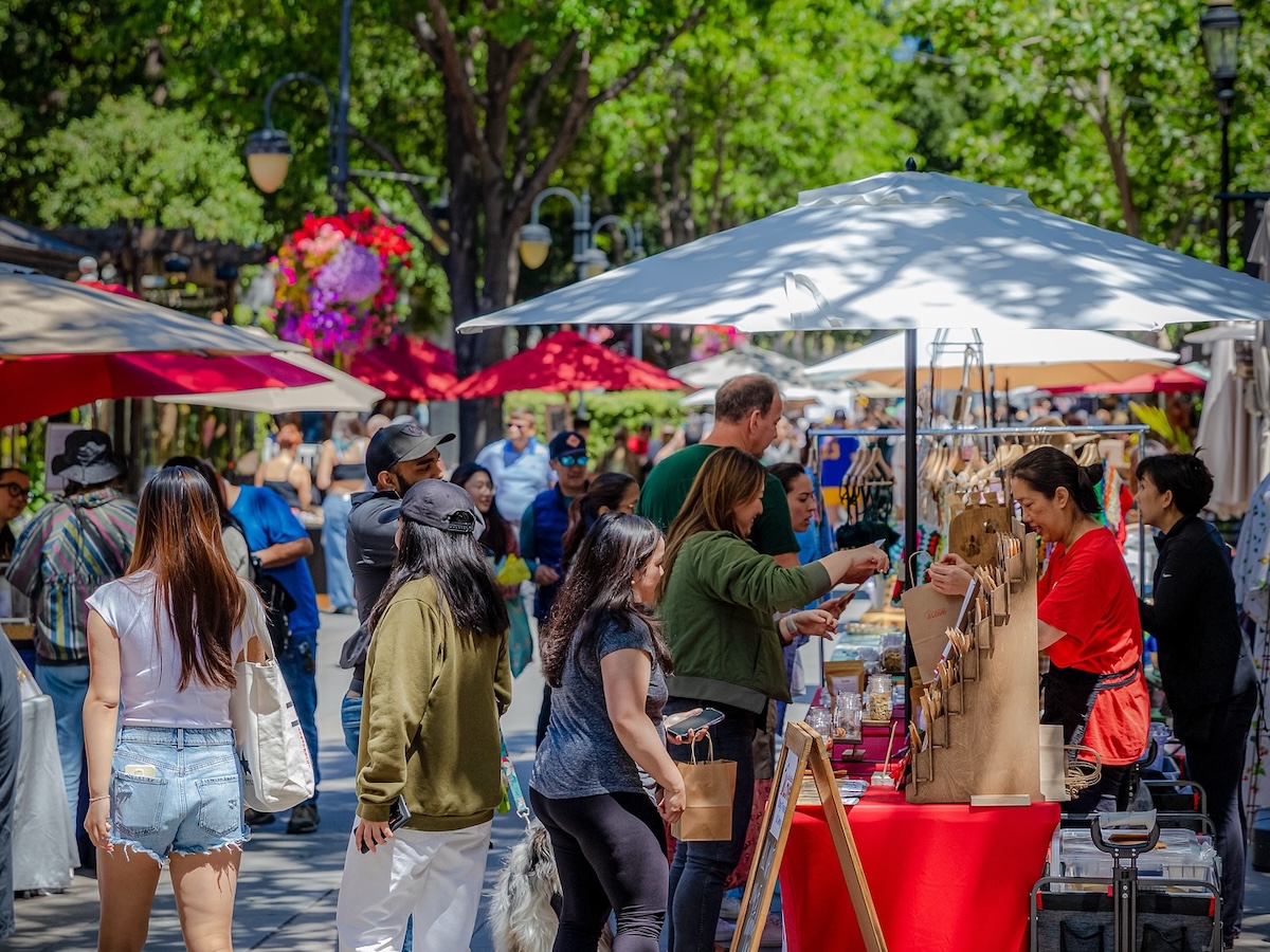 Outdoor market with umbrellas, vendor stalls and shade trees