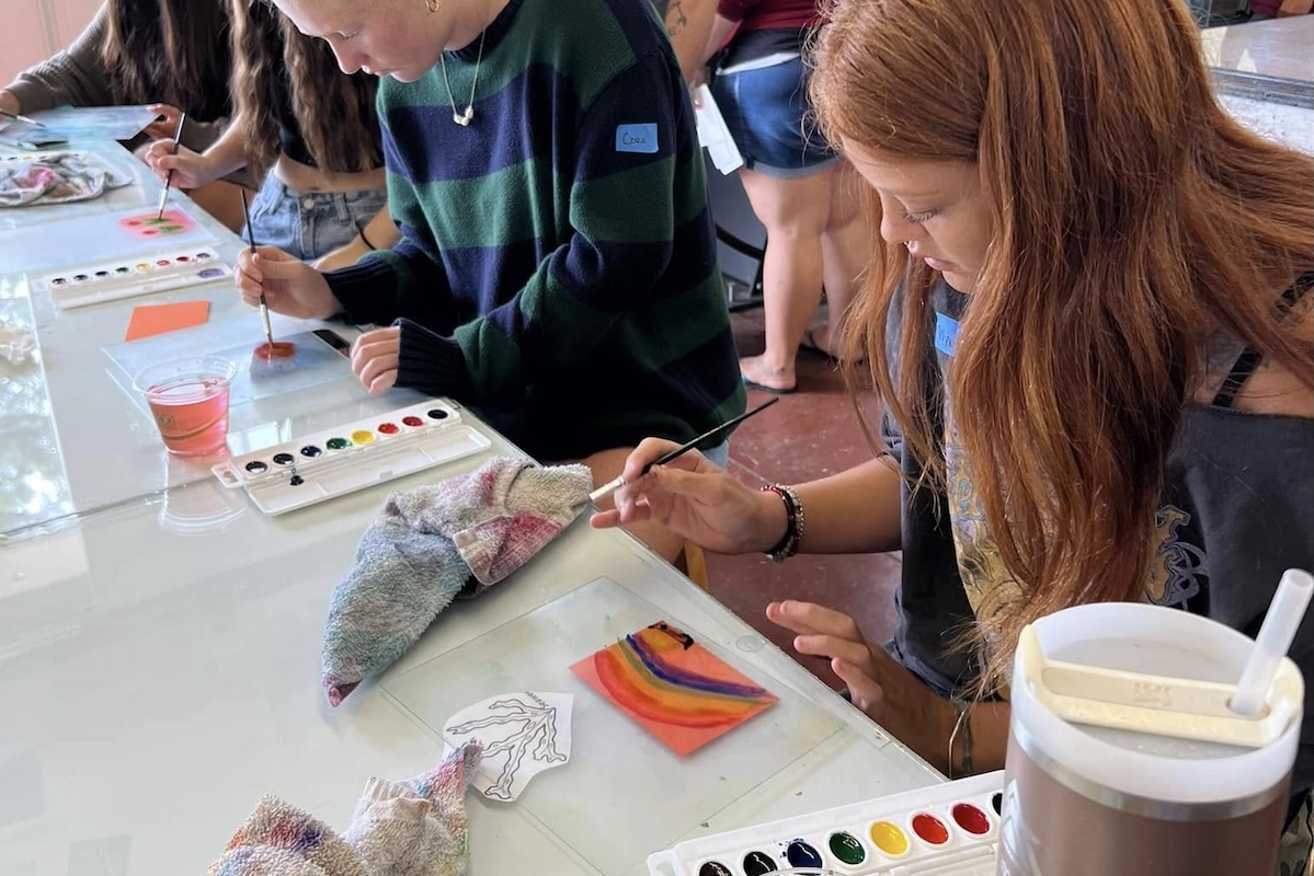 Teens focus on watercolor painting at a table.