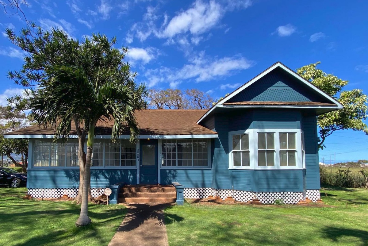 A teal building on a bright green lawn, trees and a very blue sky.