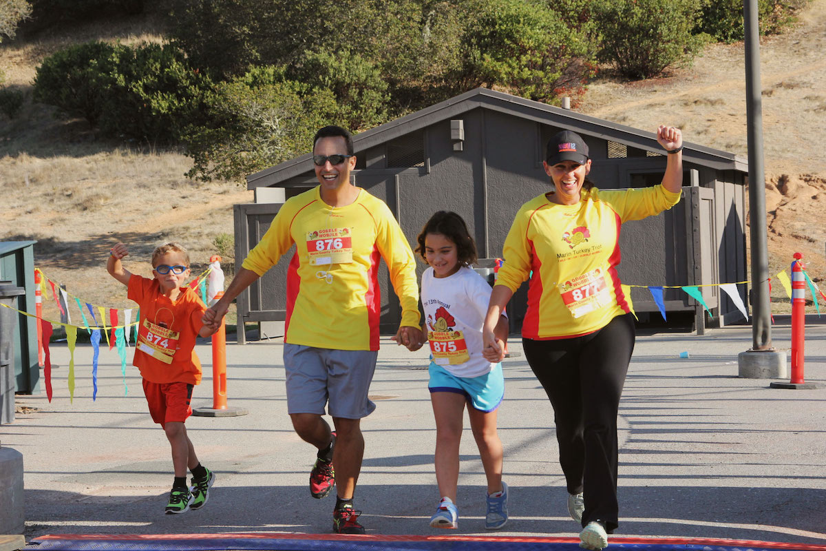Family holding hands and crossing finish line at North Bay's Bank of Marin Turkey Trot Race, happening in November