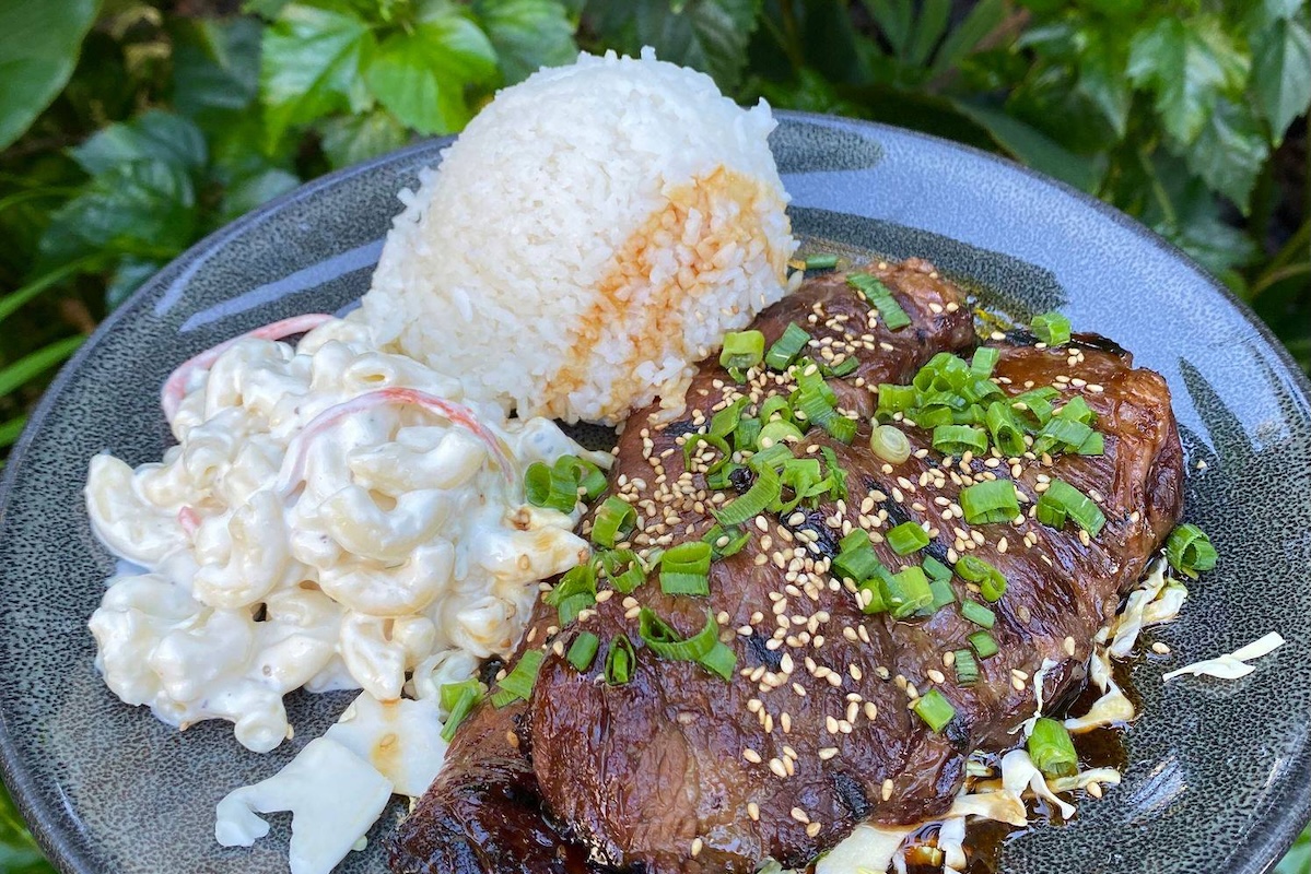 A plate held outside, with steal rice, macaroni salad and topped with green onions and sesame seeds.