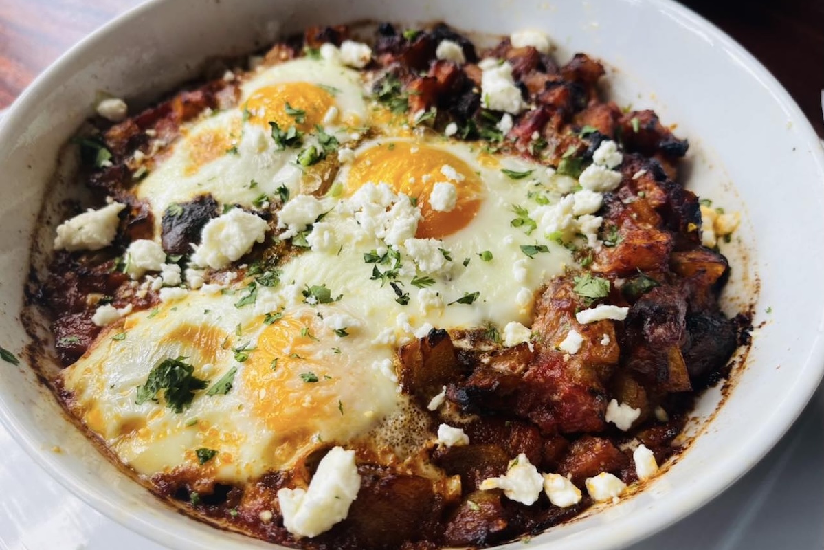 A bowl of shakshouka with eggs and crumbled cheese and herbs on top.