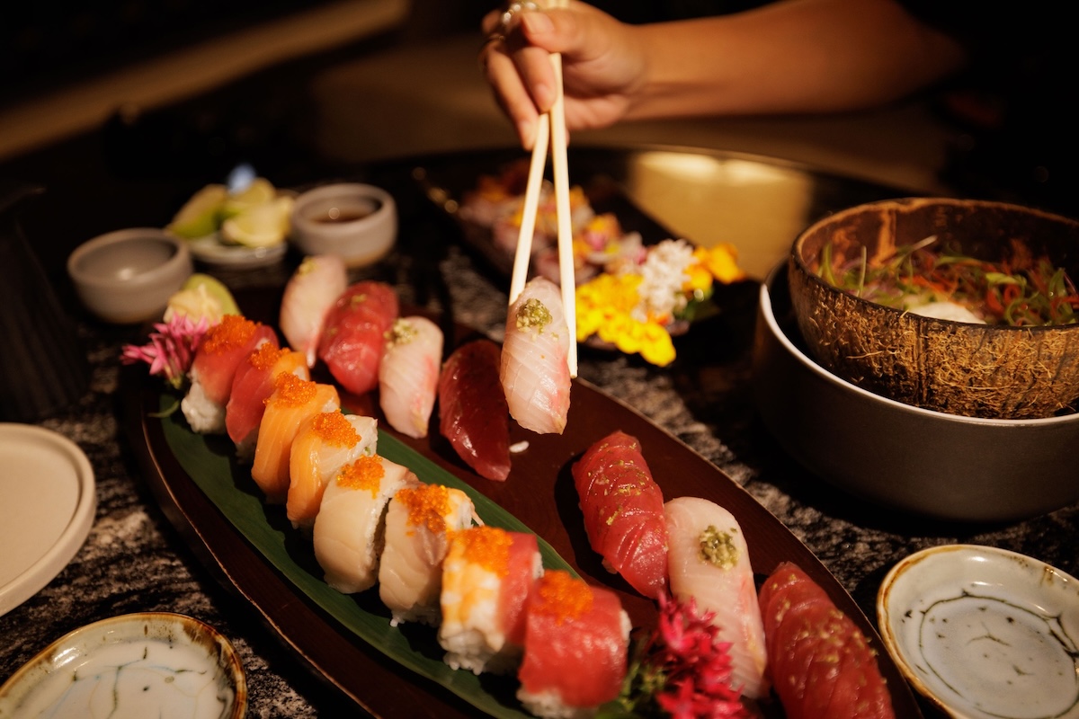 A plate of various pieces of sushi as someone picks one up with chopsticks.