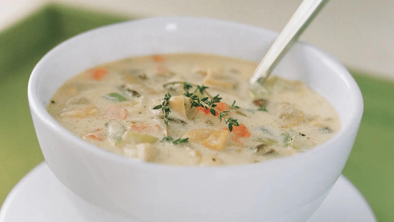 A close-up of a white bowl filled with creamy vegetable soup, perfect for warming up after enjoying the best things to do in Sonoma this January. The soup contains visible chunks of carrots, celery, and potatoes and is garnished with a sprig of fresh thyme. A spoon is placed in the bowl, ready for eating.