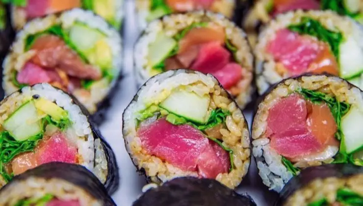 Close-up of several sushi rolls, each filled with vibrant ingredients, including raw fish (pink and red tuna), avocado, cucumber, rice, and greens, all wrapped in seaweed. The sushi pieces are uniformly arranged, showcasing a colorful and fresh appearance that reminds one of the best sushi Kauai has to offer.