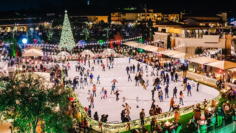 Festive outdoor ice skating rink at night, surrounded by holiday lights and decorations, including a large Christmas tree. Skaters of all ages glide on the ice, while spectators watch from the sides. Stalls and tents border the rink, adding to the lively atmosphere—one of the best things to do in Napa Valley this January.