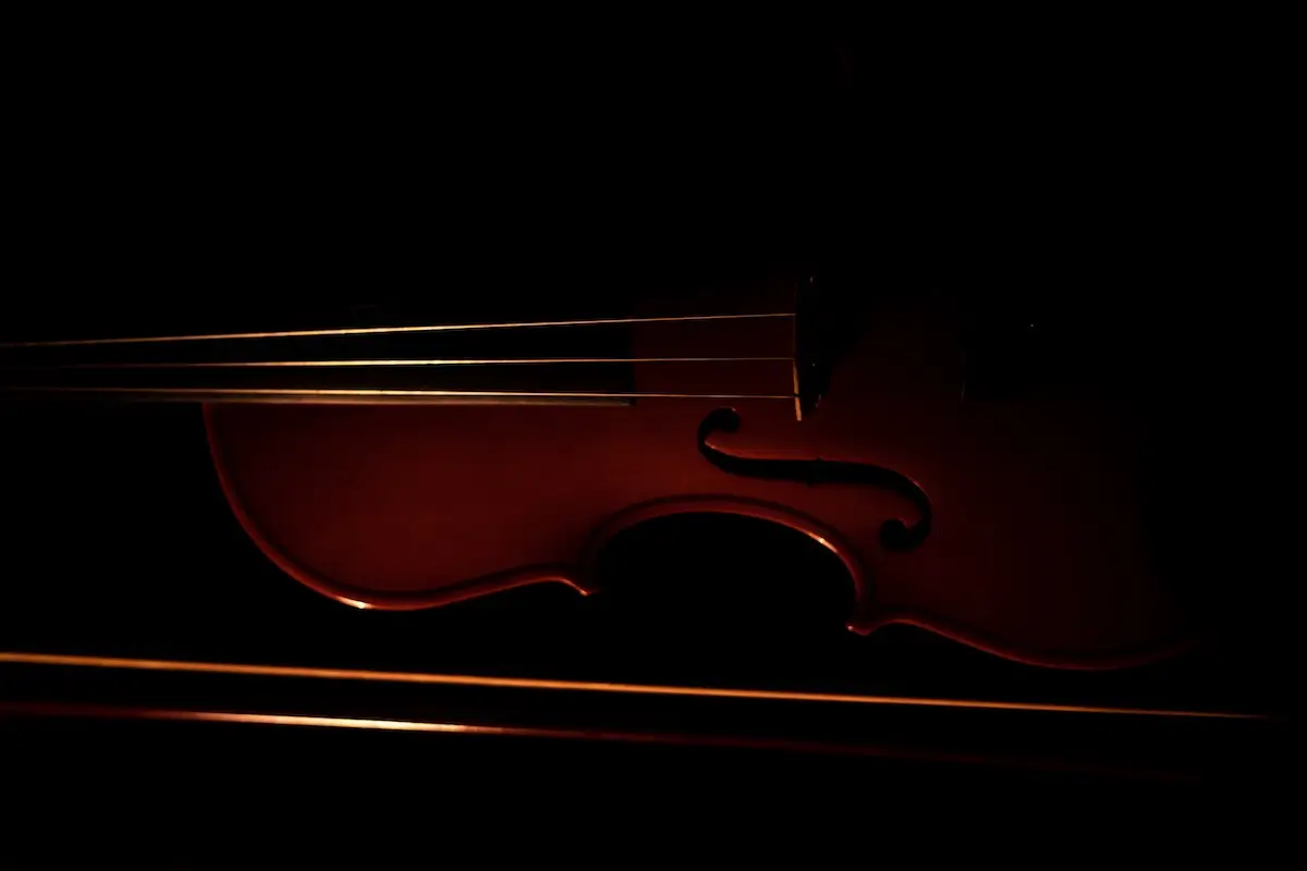 A close-up image of a violin in low light. The wooden body of the violin is illuminated with subtle, warm lighting, highlighting its curves and strings against a dark background, creating a dramatic and elegant effect—a scene reminiscent of the best things to do on Monterey Peninsula in November.