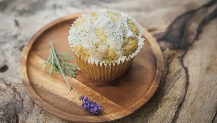 A frosted muffin sits on a wooden plate next to a small sprig of lavender and a purple flower, evoking the serene charm of the Big Island. The background is a rustic wooden surface.