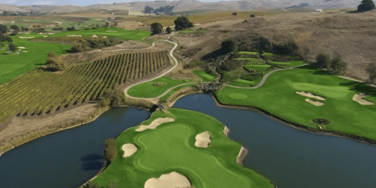 Aerial view of a picturesque golf course surrounded by expansive vineyards and rolling hills. One of the best golf courses in the greater Bay Area, it features lush green fairways, sand bunkers, and several water hazards, with neatly manicured paths winding through the landscape.