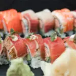 A close-up of a beautifully arranged sushi platter, perfect for dinner in Paia and Hana Maui, featuring various types of sushi rolls, including slices of tuna, salmon, and other fish topped with decorative microgreens. Wasabi and pickled ginger are placed in the foreground.