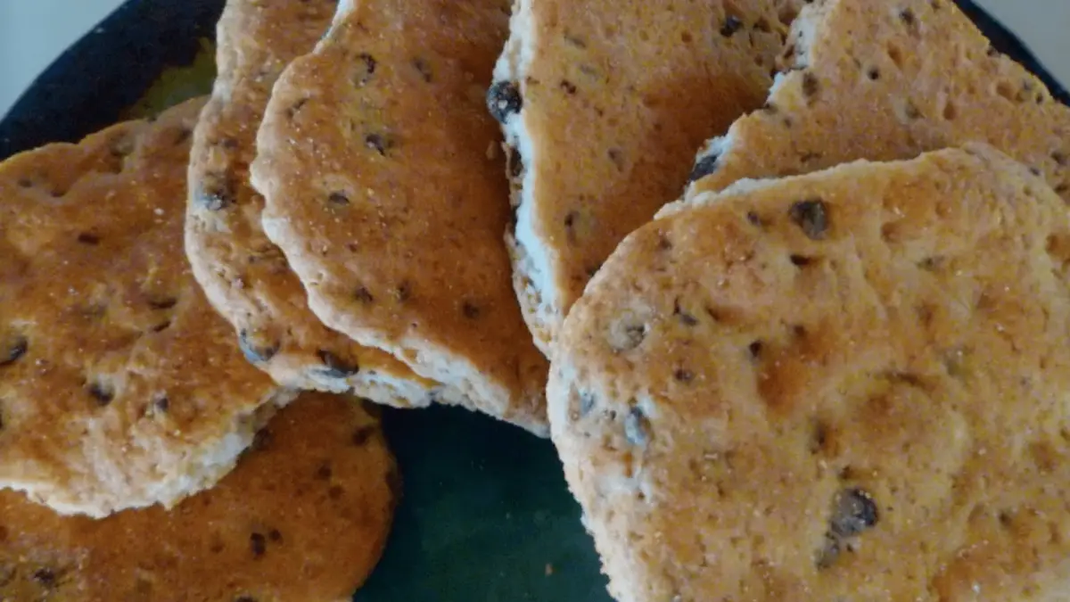 A close-up image of a plate filled with homemade Welsh cakes, speckled with currants or raisins. The round cakes are slightly browned, their soft and crumbly texture inviting closer inspection. Ideal for those who appreciate traditional snacks that define cultural culinary experiences.