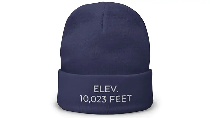 A navy blue beanie with a folded brim, featuring embroidered white text on the brim that reads, "ELEV. 10,023 FEET," perfect for your adventures as you follow Maui’s House Sun Stars Guide to Haleakalā National Park.
