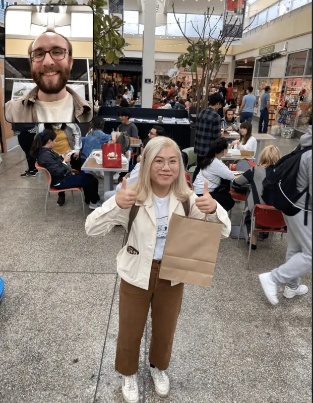 A person with long blonde hair, glasses, and a white jacket stands in a busy food court area giving two thumbs up while holding a brown paper bag. An inset shows a bearded person with glasses smiling during a video call on Gen Z's new favorite app. People are seated and walking in the background.