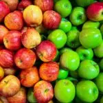 A display of fresh apples: red apples on the left and green apples on the right. The red apples have a mix of reddish and yellow hues, while the green apples are uniformly bright green. The closely packed arrangement offers a vibrant contrast, showcasing high apple rankings in quality and color.