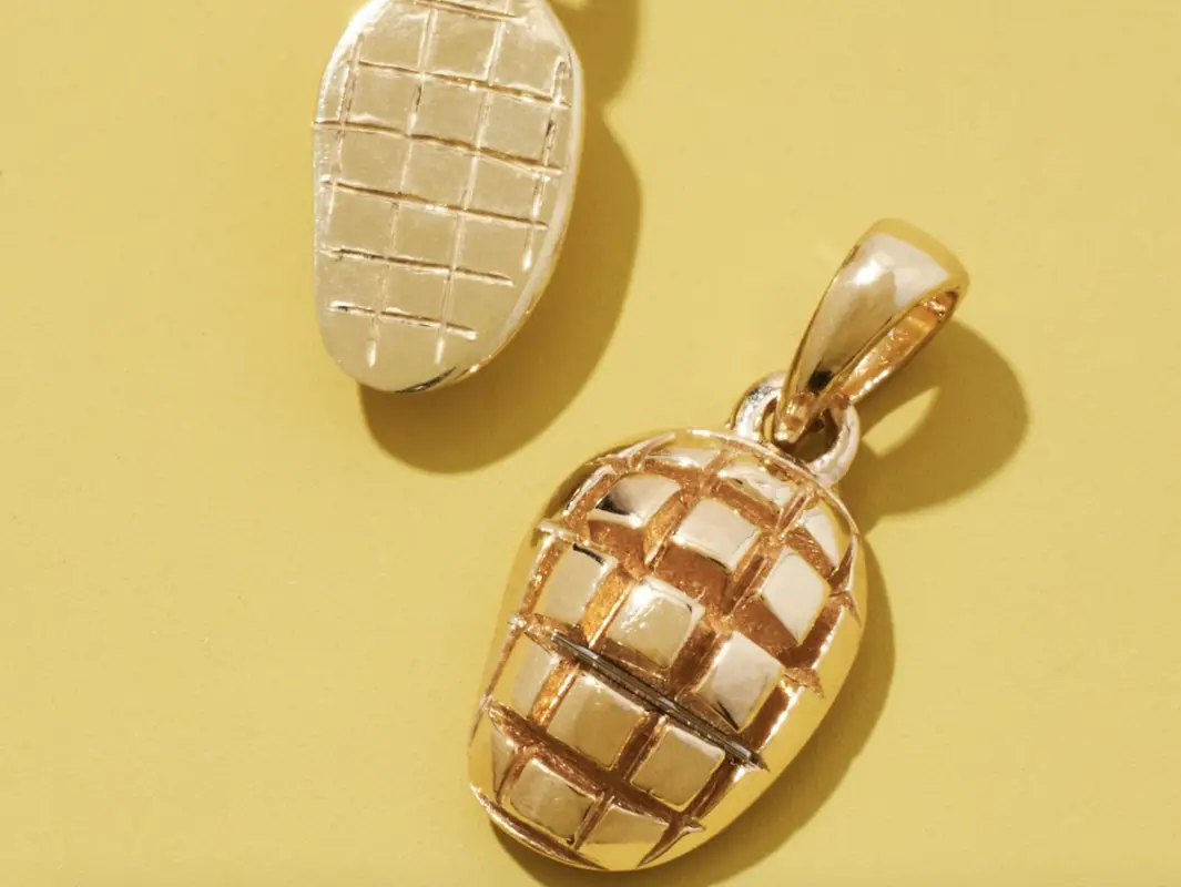 Two gold and silver pendant charms on a yellow background. Each pendant has a grid-like pattern, resembling a stylized, textured egg or oval shape. One charm is primarily gold, the other mainly silver—perfect Valentines Day gifts from Hawai'i to express your unique love.