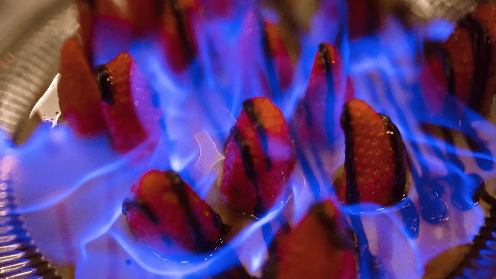 Close-up image of a dessert featuring strawberries arranged on a tray. The sliced strawberries are topped with a caramelized glaze, and blue flames elegantly dance among them, highlighting the flambé presentation—one of the best desserts Maui Wailea has to offer.