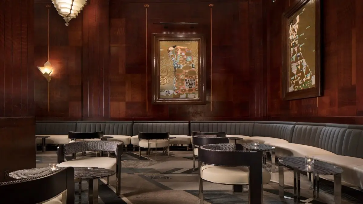 A classy bar with dark wooden panels, modern light fixtures, and art on the walls. Round tables with elegant black-and-white chairs are set along a curved, cushioned bench. Celebrate San Francisco Pride all month long with these special events in this dim and sophisticated ambiance, enhanced by a polished stone floor.