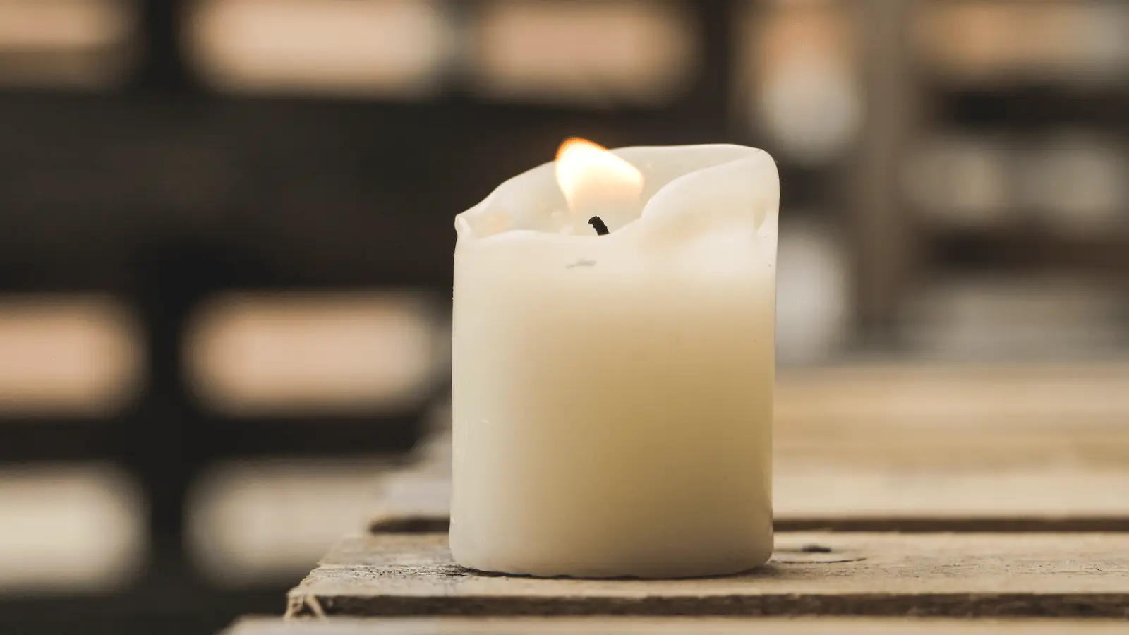 A lit white candle with a slightly melted top sits on a wooden surface. The background is blurred, emphasizing the candle's warm glow, reminiscent of the serene ambiance you'd find during Lomilomi, Hawaii’s ancient massage known for its real health benefits.