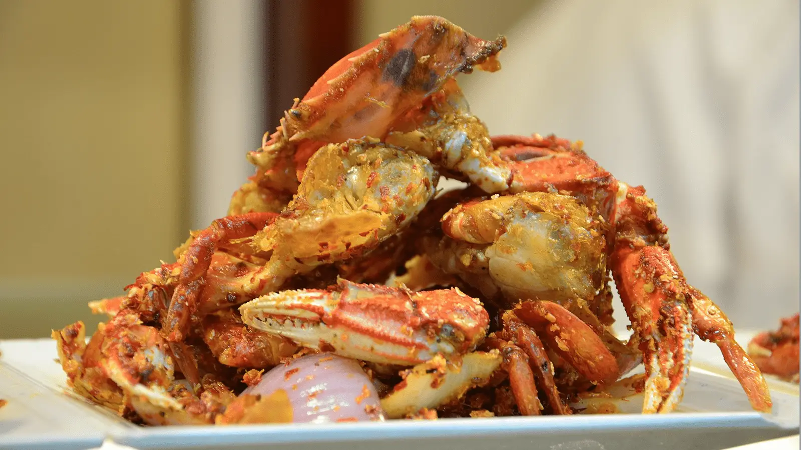 A plate of cooked crab pieces, seasoned with spices and herbs, piled high. The crab shells appear reddish-orange and are crispy, with visible seasoning. There are also visible onions and other ingredients mixed with the crab.