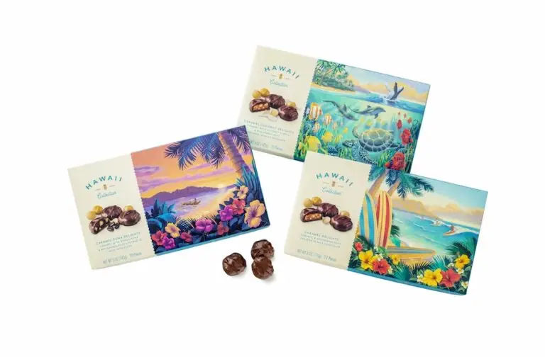 Three boxes of Hawaii Collection chocolates featuring vibrant tropical artwork on the covers await you at Duty Free Shops Hawaii. Each box showcases different Hawaiian scenes, including beaches, palm trees, and surfboards. Several chocolate-covered pieces are placed in front of the boxes.