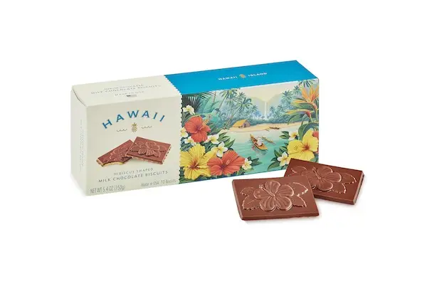 A box of Hawaii-branded milk chocolate biscuits, available at Duty Free Shops Hawaii, features tropical floral designs and an image of a boat on blue water. Two chocolate biscuits are placed outside the box, each embossed with a hibiscus flower design.