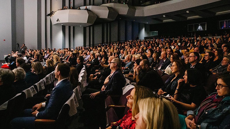 An auditorium filled with many seated people, attentively facing the front. The audience comprises a diverse group, dressed in formal and semi-formal attire, likely attending one of the best annual events in Napa Valley. The setting appears to be a conference or formal presentation. The room is well-lit.