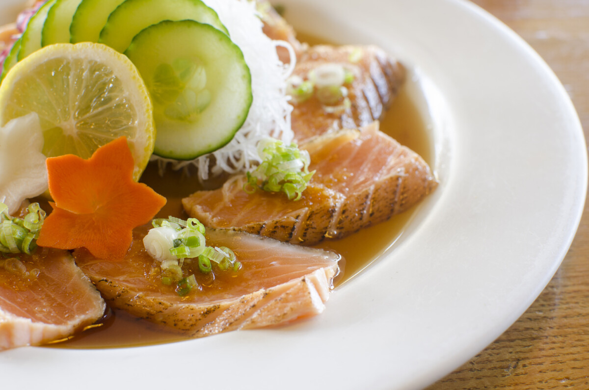 A plate of thinly sliced seafood in a sauce and topped with vermincelli noodles, thin cucumbers, star-shaped carrot slices and more.