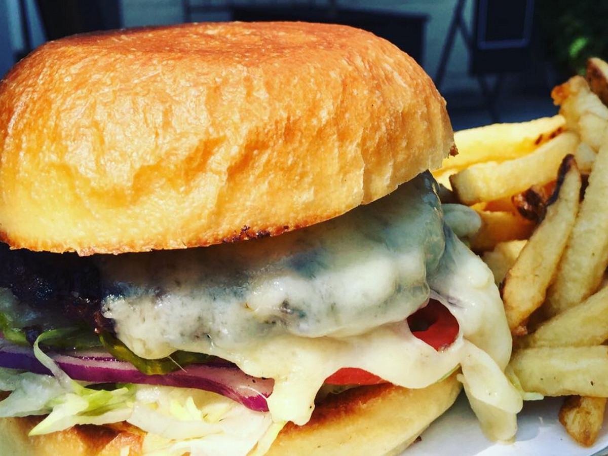 Close-up of a cheeseburger with a toasted bun, melted cheese, lettuce, onions, and tomato. The burger is accompanied by a side of golden French fries. The background is blurry, highlighting the focus on the meal—potentially one of the Best Burgers in Marin.