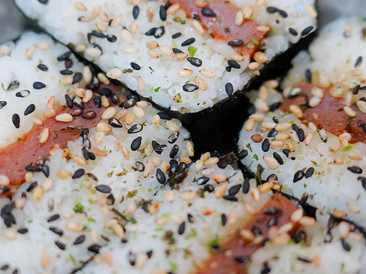 Close-up of sliced sushi rolls topped with white and black sesame seeds. The rolls contain rice and a pink filling, likely tuna, wrapped in seaweed. Several pieces are clustered together with a detailed view of the texture of the ingredients—truly the Best Sushi in Marin.