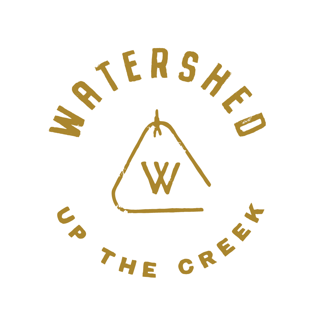 A circular logo with the words "Watershed Up the Creek" written around a central triangular design. Inside the triangle, there is a stylized "W" letter. The text and design are in a gold color on a black background, capturing the essence of Mill Valley Restaurant Rally and Bay Area brunch vibes.