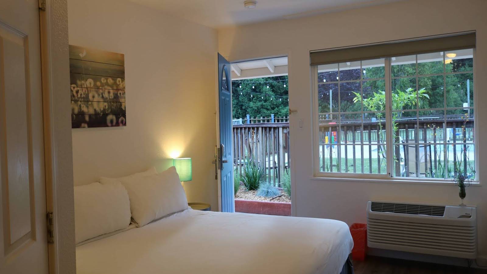 Casa Secoya room, with white bed, green lamp, AC unit, and view to outside patio with lights.