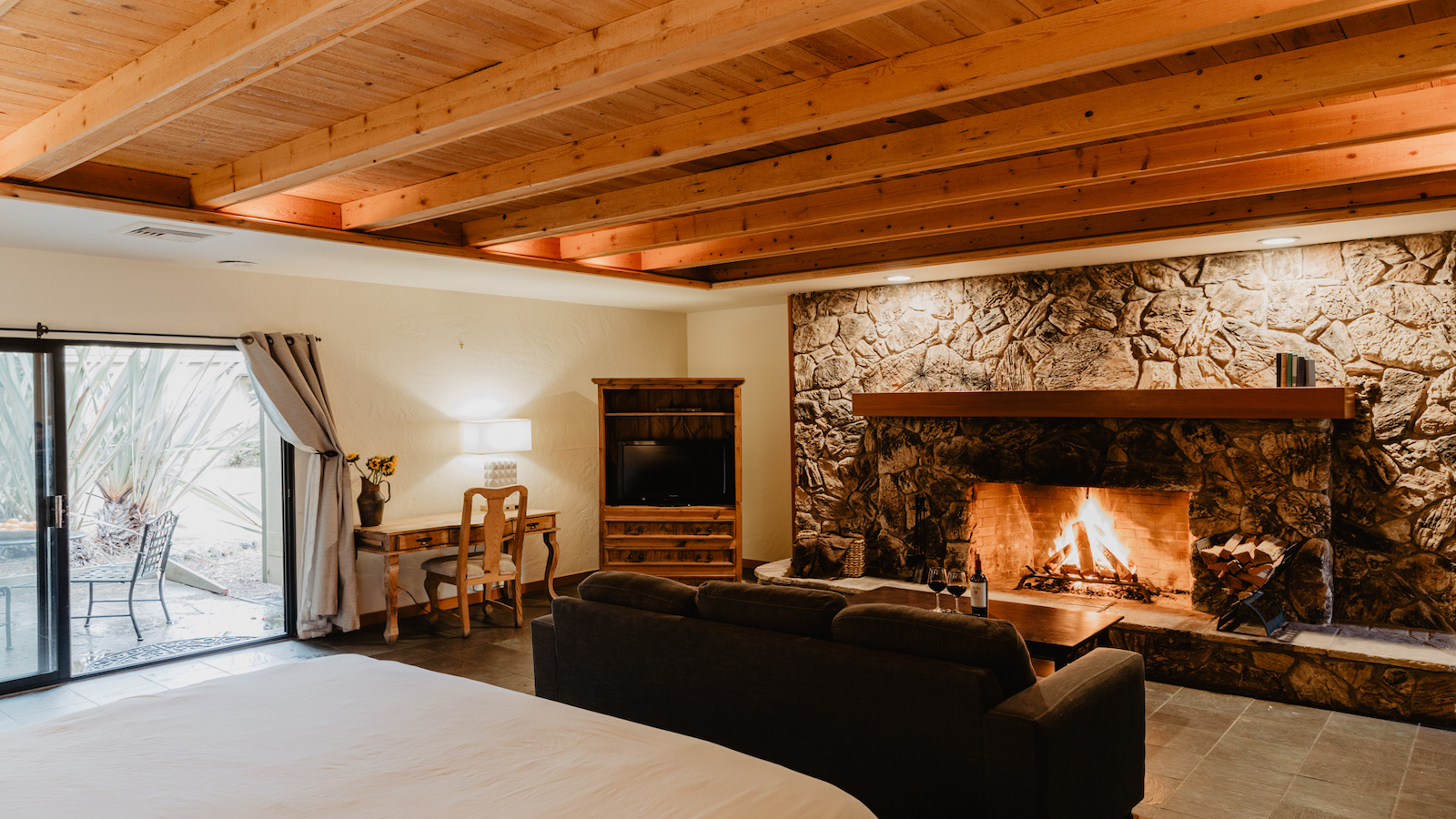 Hotel room with ceiling beams, stone fireplace, and black couch.