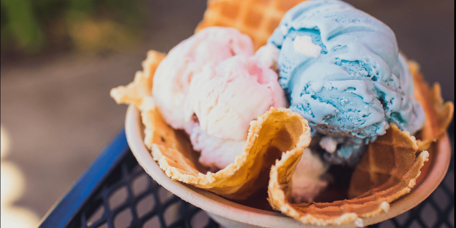 A close-up of a bowl with two scoops of ice cream, one pink and one blue, served in a waffle bowl. The image captures the creamy texture and vibrant colors of the ice cream against the crisp, golden-brown waffle, creating an inviting and delicious scene.