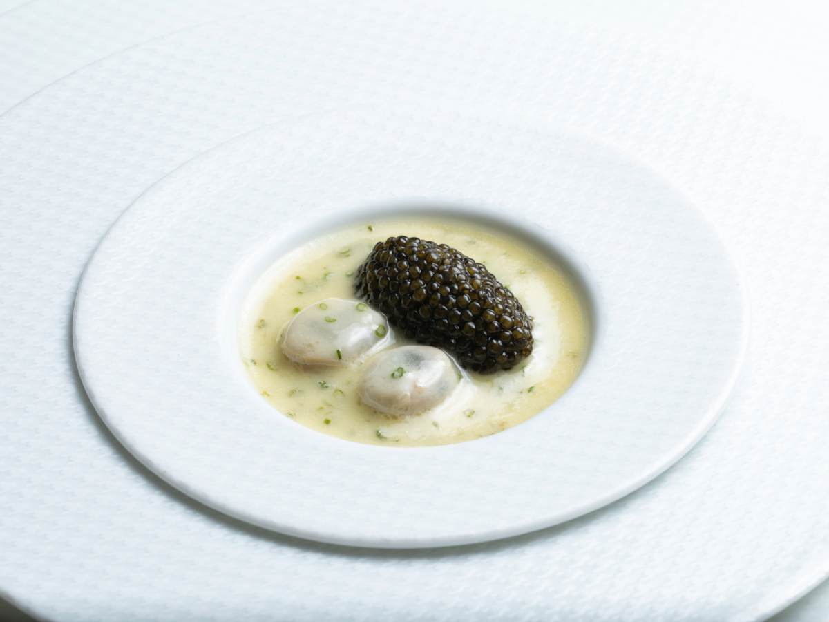 A white dish from Napa features a creamy sauce with herbs, topped with two poached oysters and a generous portion of black caviar. The plate has a textured, circular design around the rim, and the elegant presentation suggests a gourmet dish typical of Michelin-Rated Restaurants.