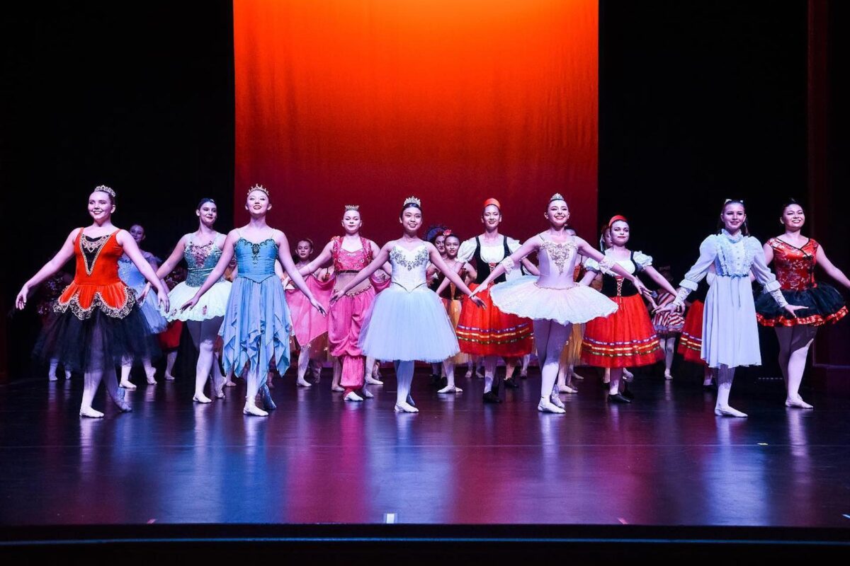 Dancers in the Nutcracker stand on a stage to bow, with a red backdrop.