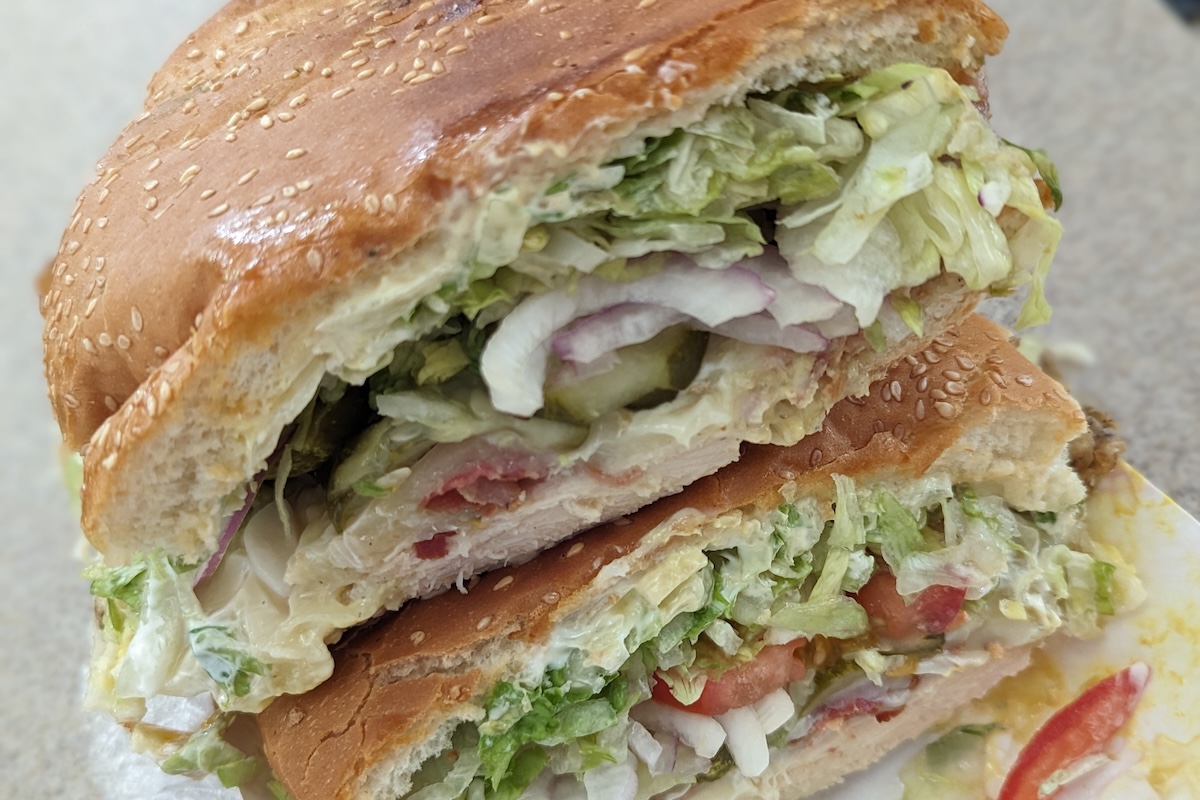 A stack of two sandwich halves with lettuce, mayo, onions, tomato and more.
