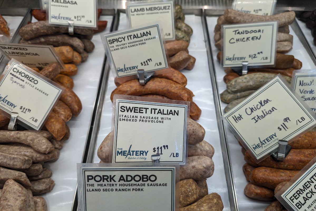A glass case display of various sausage flavors with signs indicating the flavors.