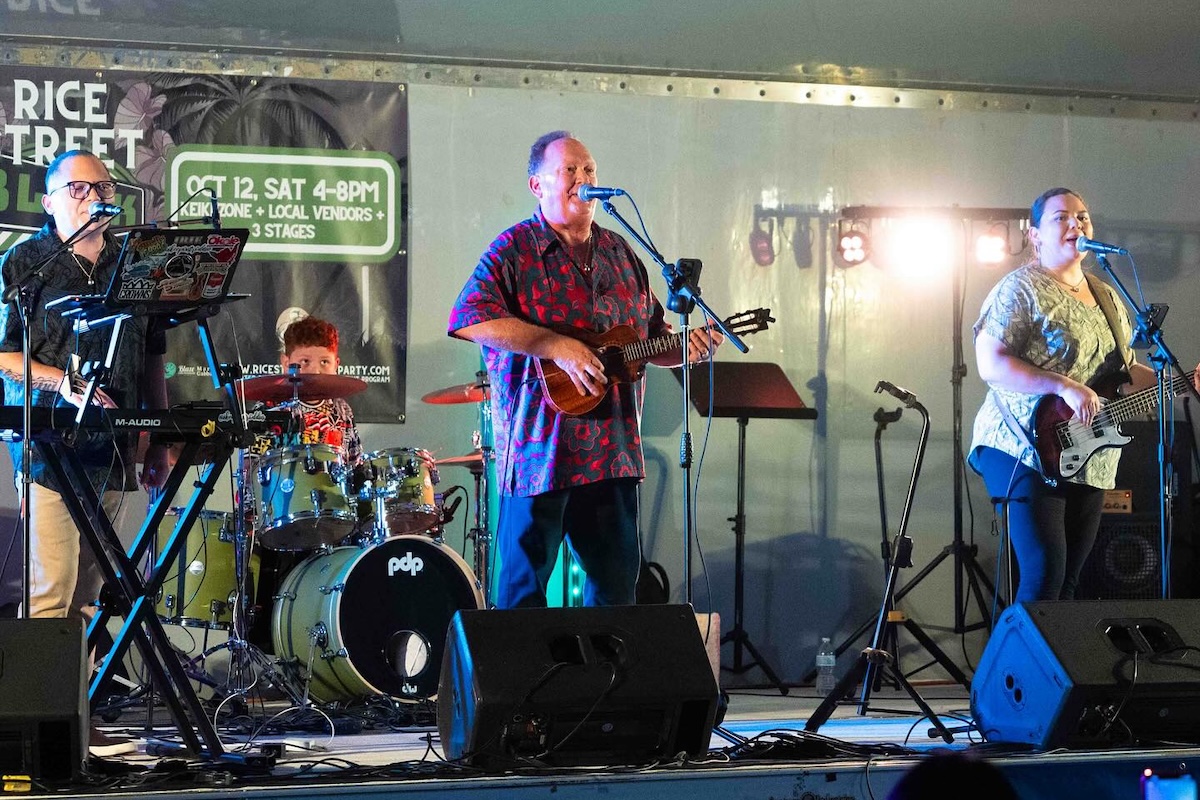 A band including a drummer, guitarist, keyboard player and ukulele player perform on stage.